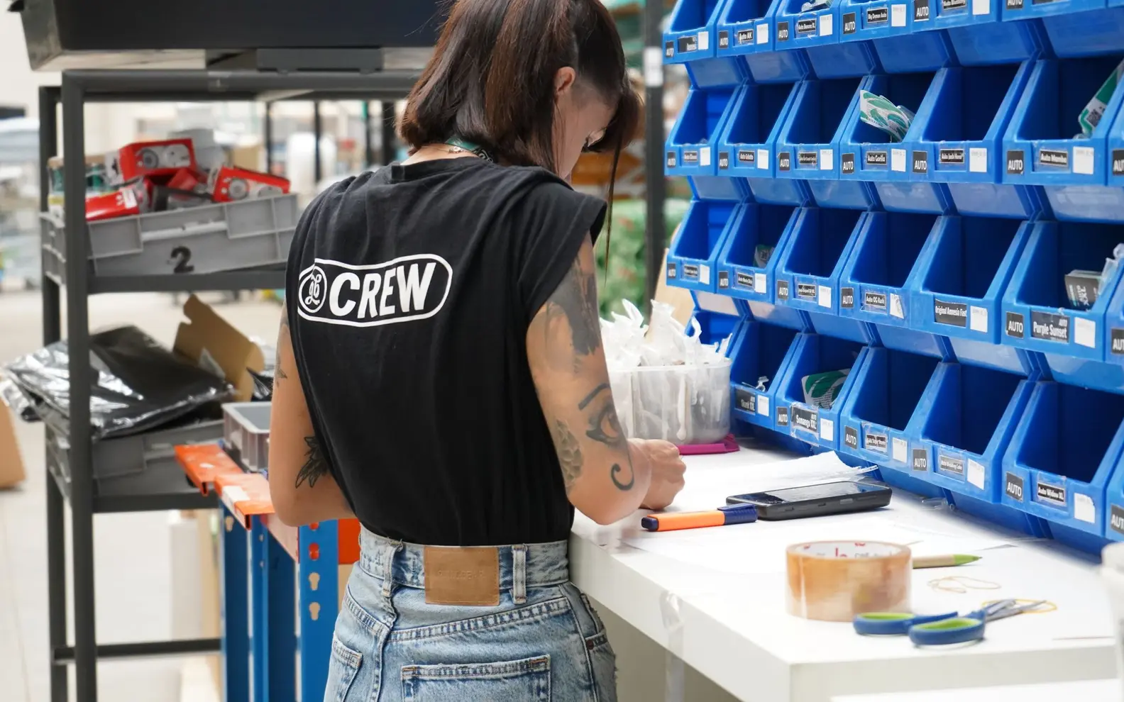 Warehouse specialist checking organised component inventory in labelled storage bins with a clipboard