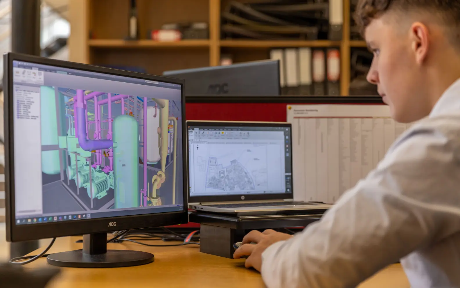 Engineer reviewing detailed CAD and model information across dual computer monitors in a technical office