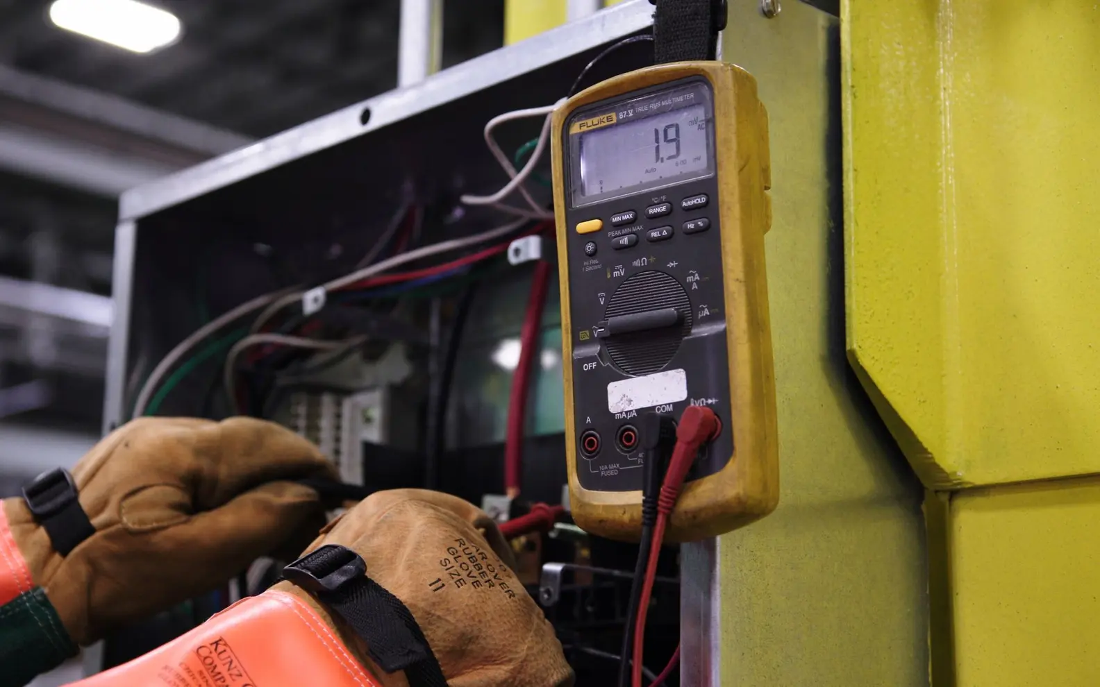 Electrical technician testing an industrial control panel with a digital multimeter