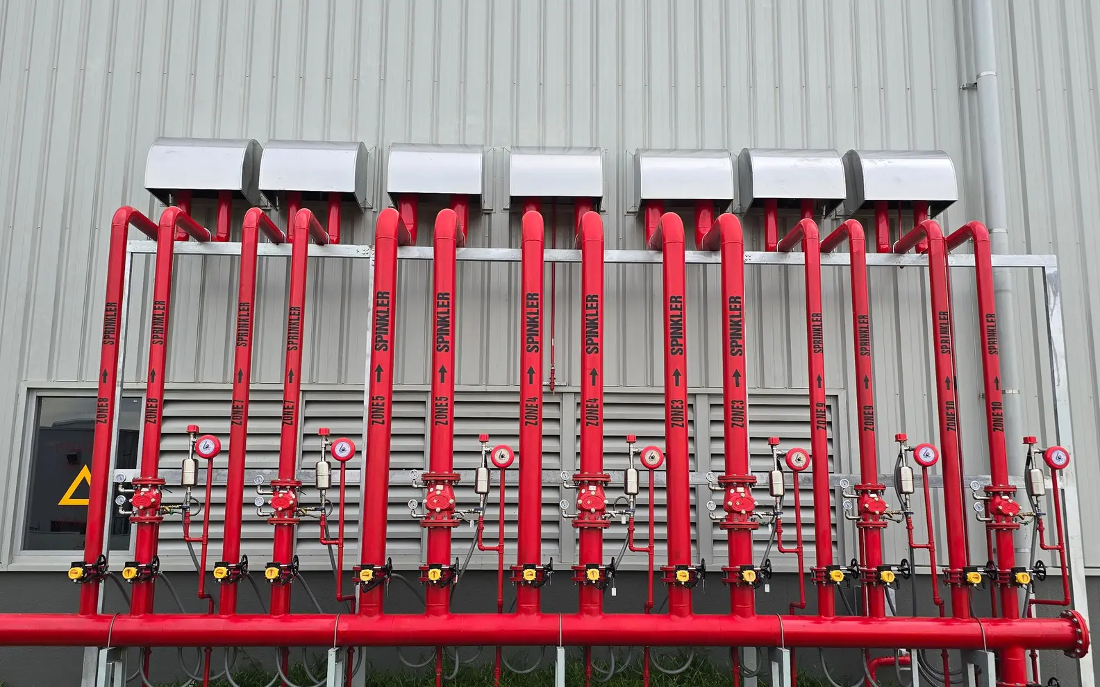 Red industrial fire-sprinkler pipework and control valves installed along a factory wall