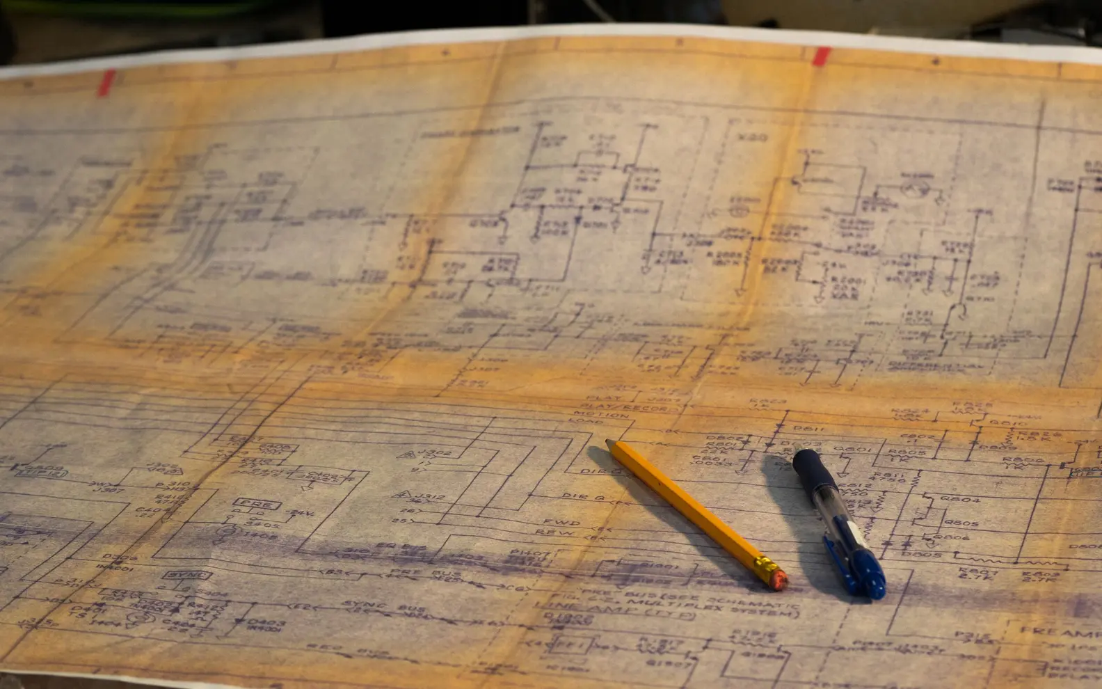 Detailed legacy engineering drawing spread across a drafting table with pencil and pen