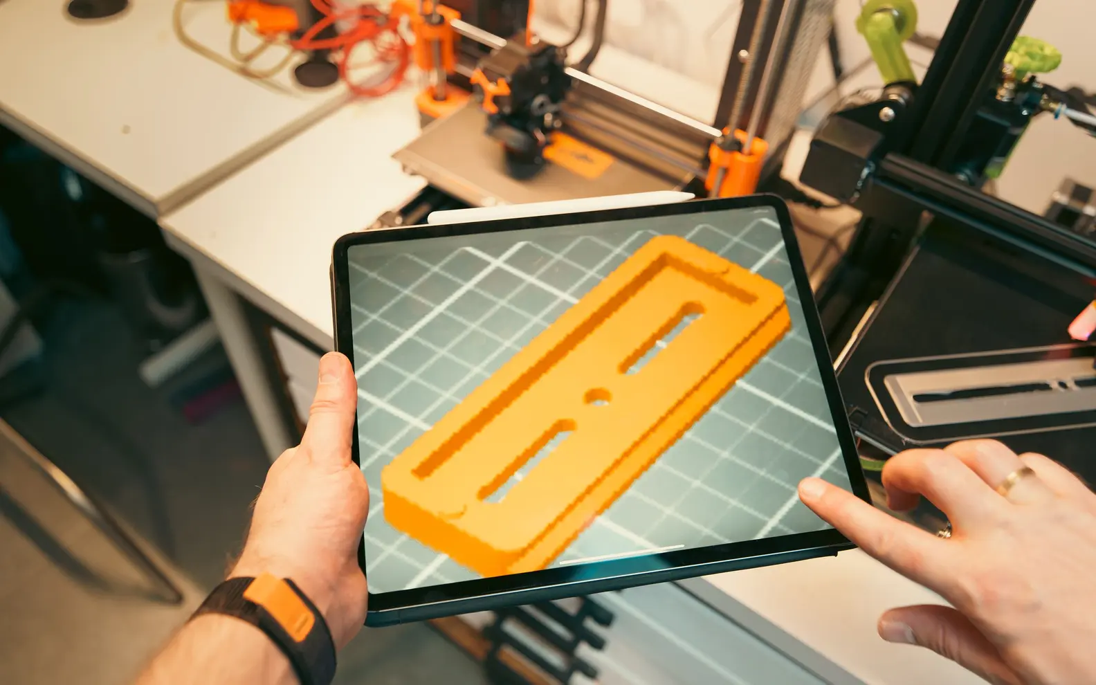 Designer reviewing a three-dimensional component model on a tablet beside prototype equipment