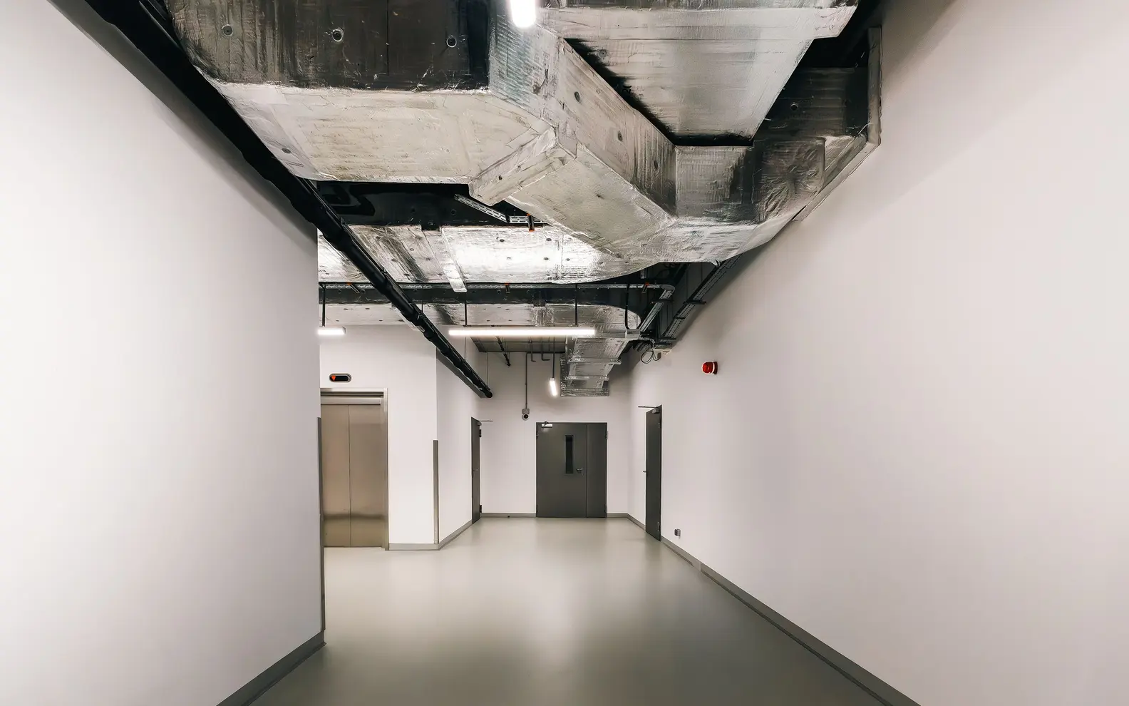 Modern commercial corridor with exposed coordinated ductwork, pipework, lighting and building services