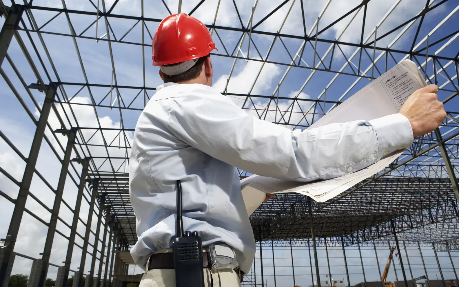 Structural engineer reviewing construction drawings beneath an erected steel building frame
