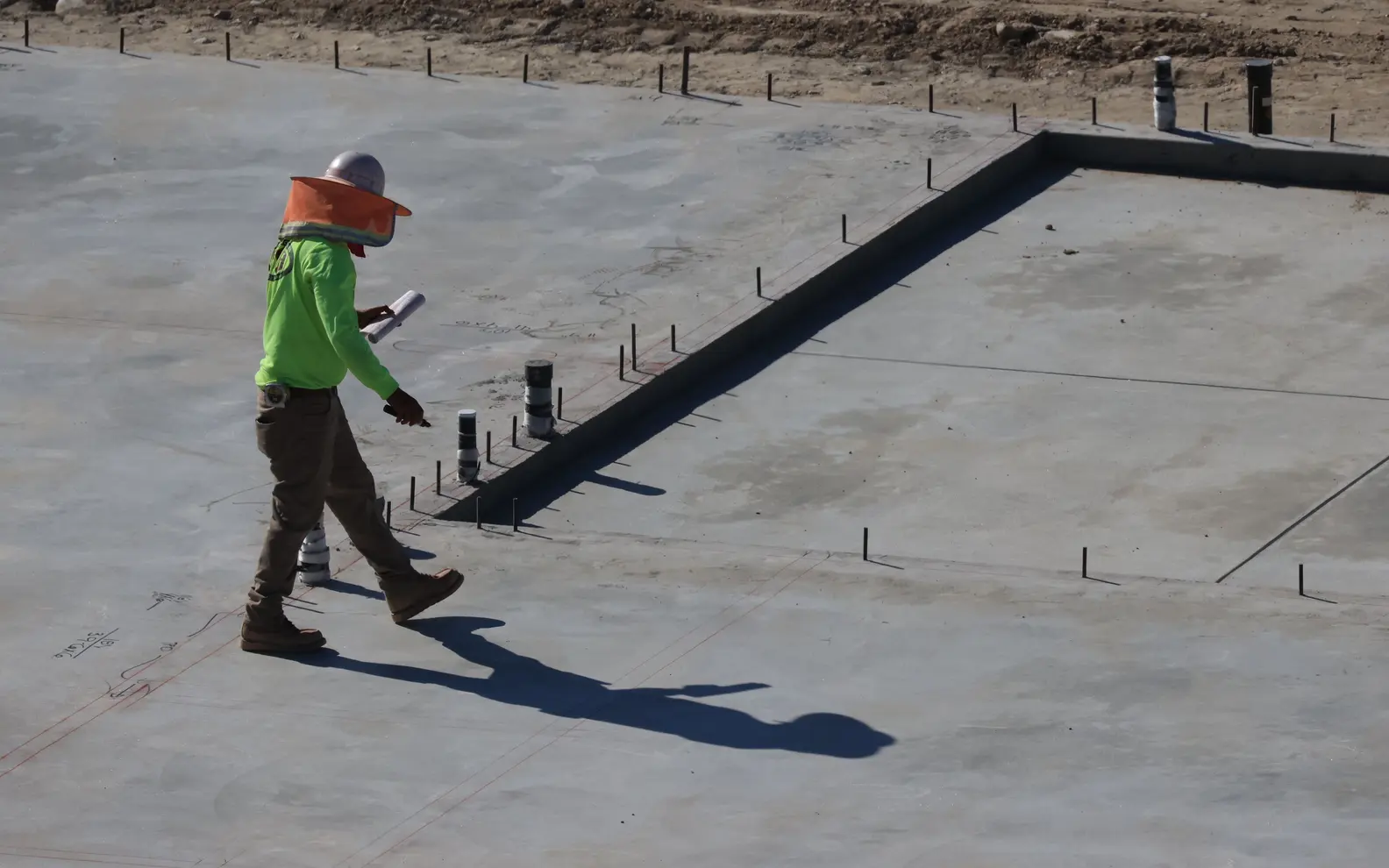 Site engineer inspecting a completed concrete foundation slab against construction drawings
