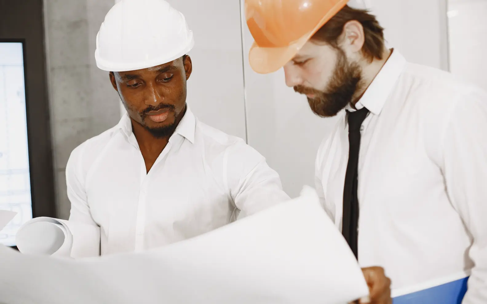 Two construction engineers reviewing a large set of technical drawings together