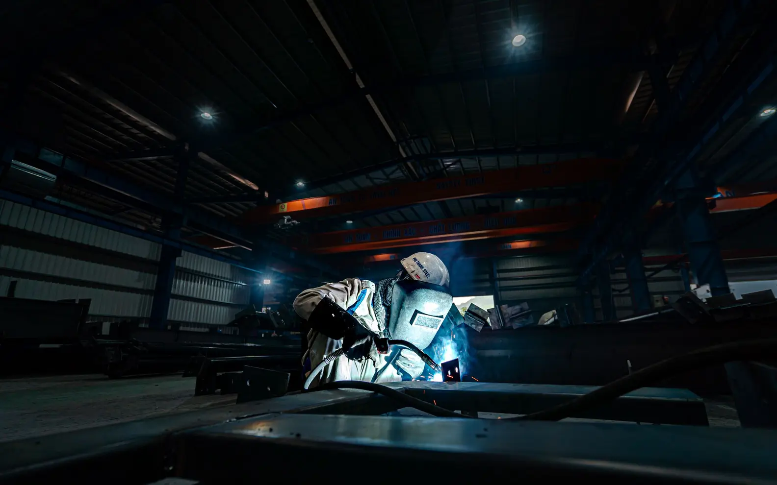 Welder joining a large steel structure inside an industrial fabrication workshop